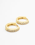Two gold-colored CZ huggie earrings arranged diagonally on white, showing the hinged closures.
