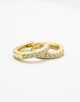 Two overlapping gold-colored CZ huggie earrings on a white background, showing the stone-lined fronts.