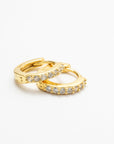 A pair of gold-colored huggie earrings with cubic zirconia stones, displayed against a white background.