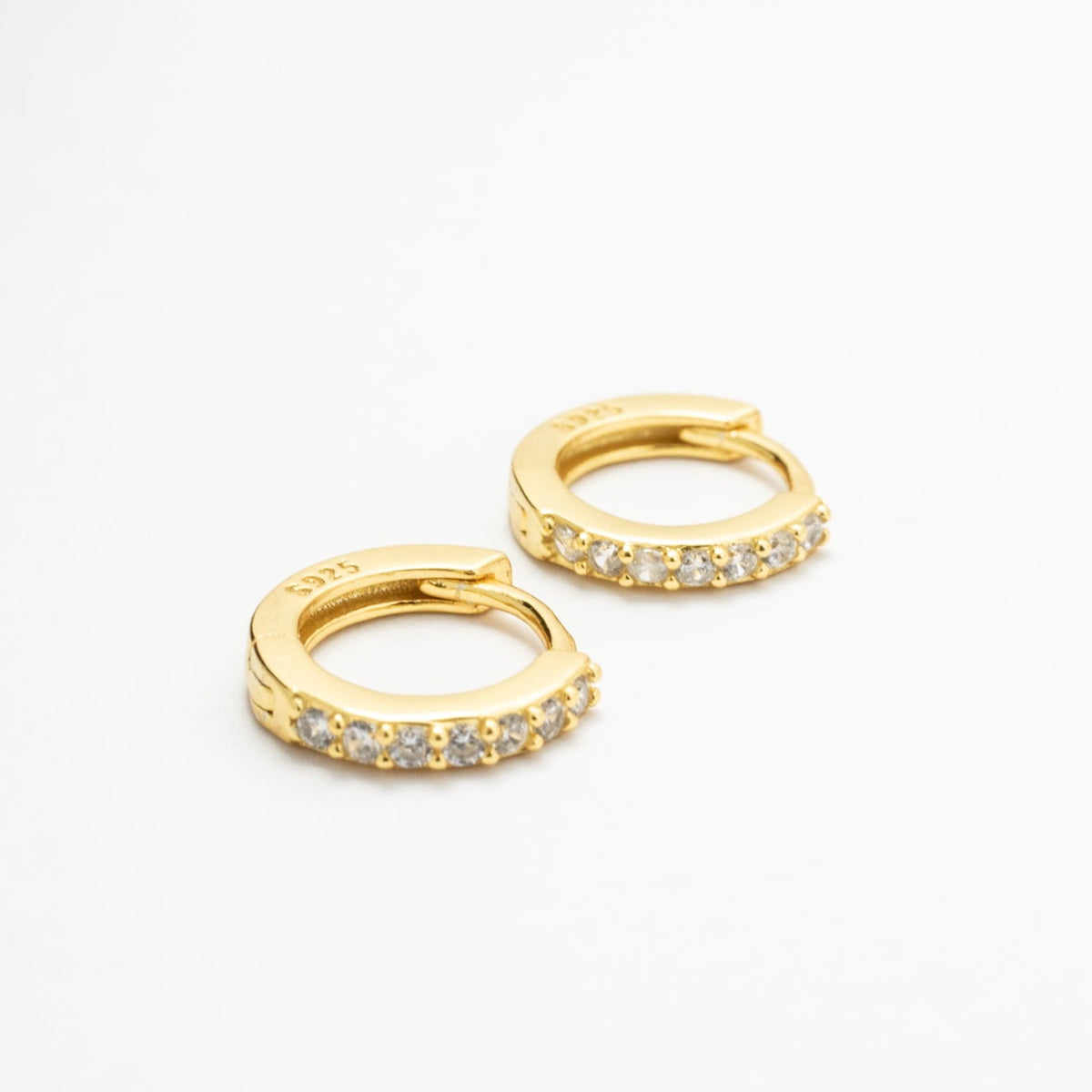 Two gold-colored CZ huggie earrings arranged diagonally on white, showing the hinged closures.