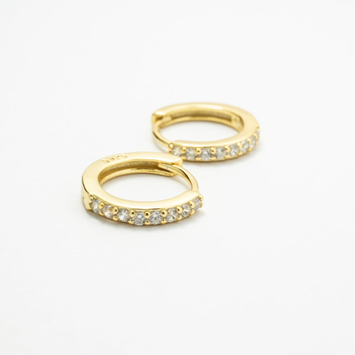 Gold-colored CZ huggie earrings on white, with one hoop in front of the other.