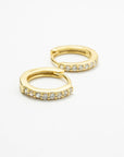 Gold-colored CZ huggie earrings on white, with one hoop in front of the other.