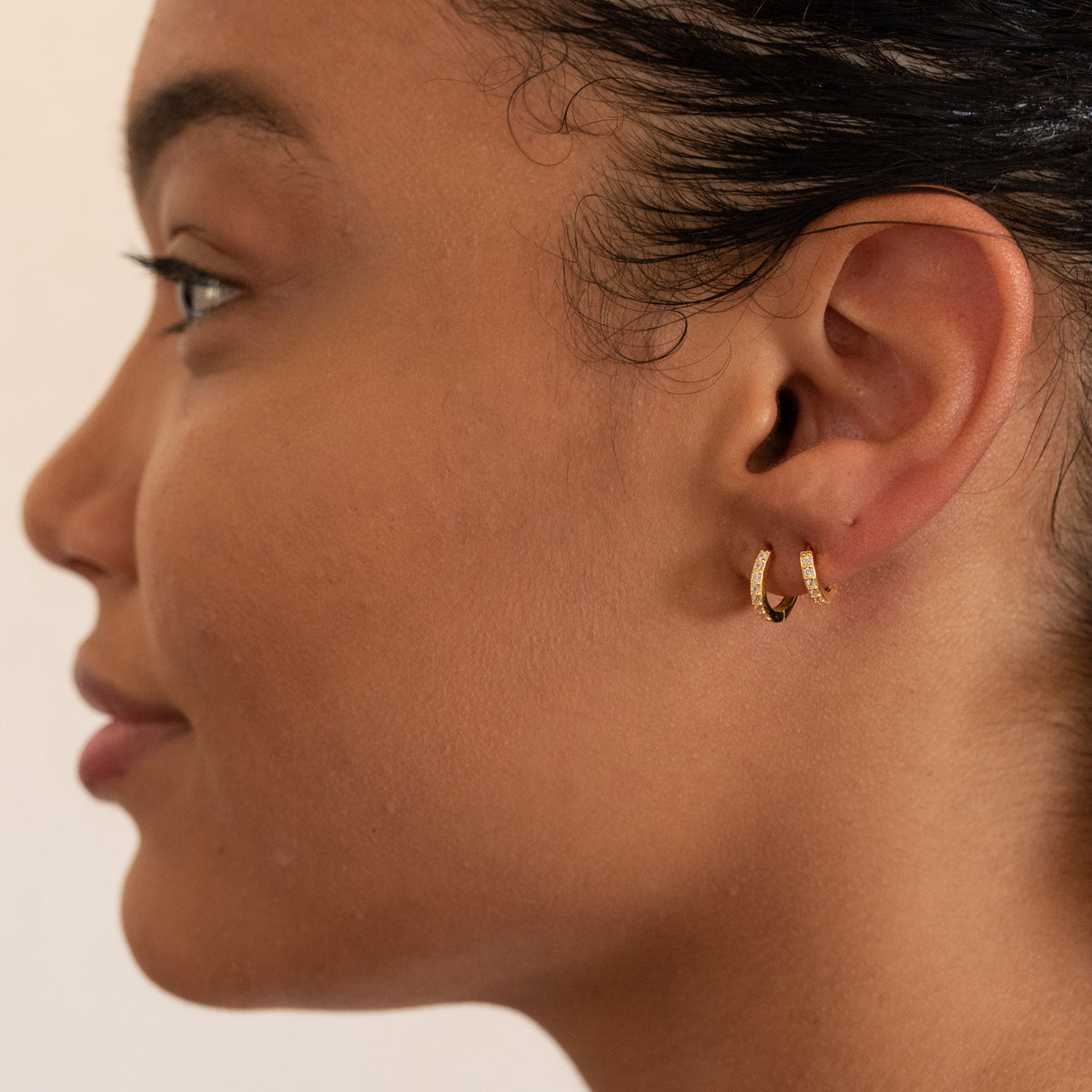  Model wearing two gold-colored CZ huggie earrings in adjacent lobe piercings, side profile view.