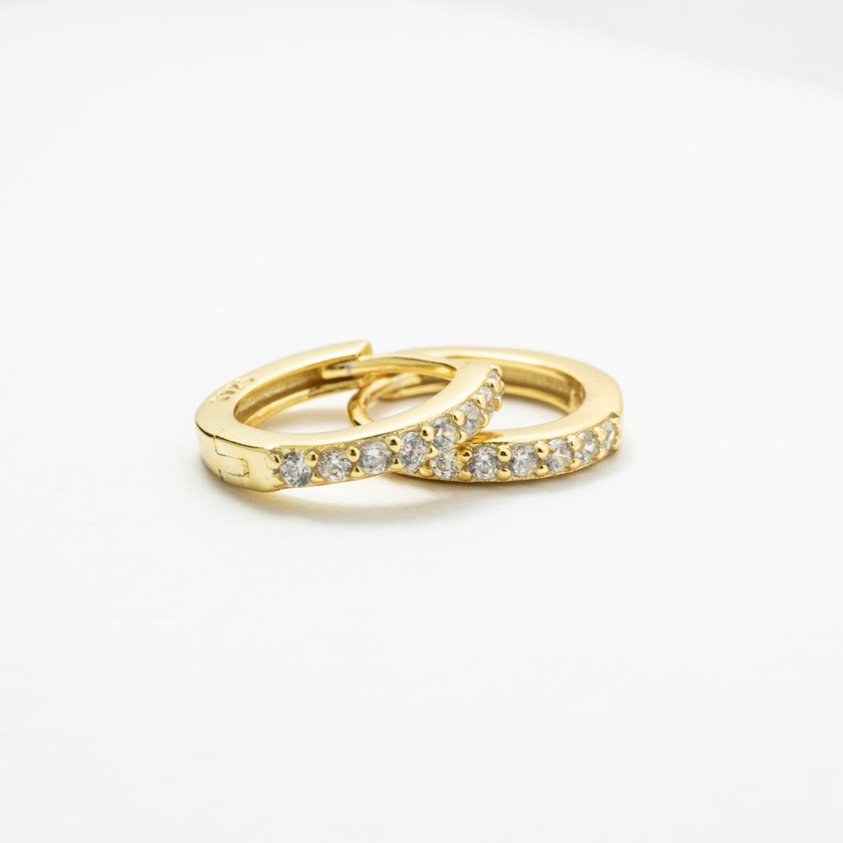 Two overlapping gold-colored CZ huggie earrings on a white background, showing the stone-lined fronts.